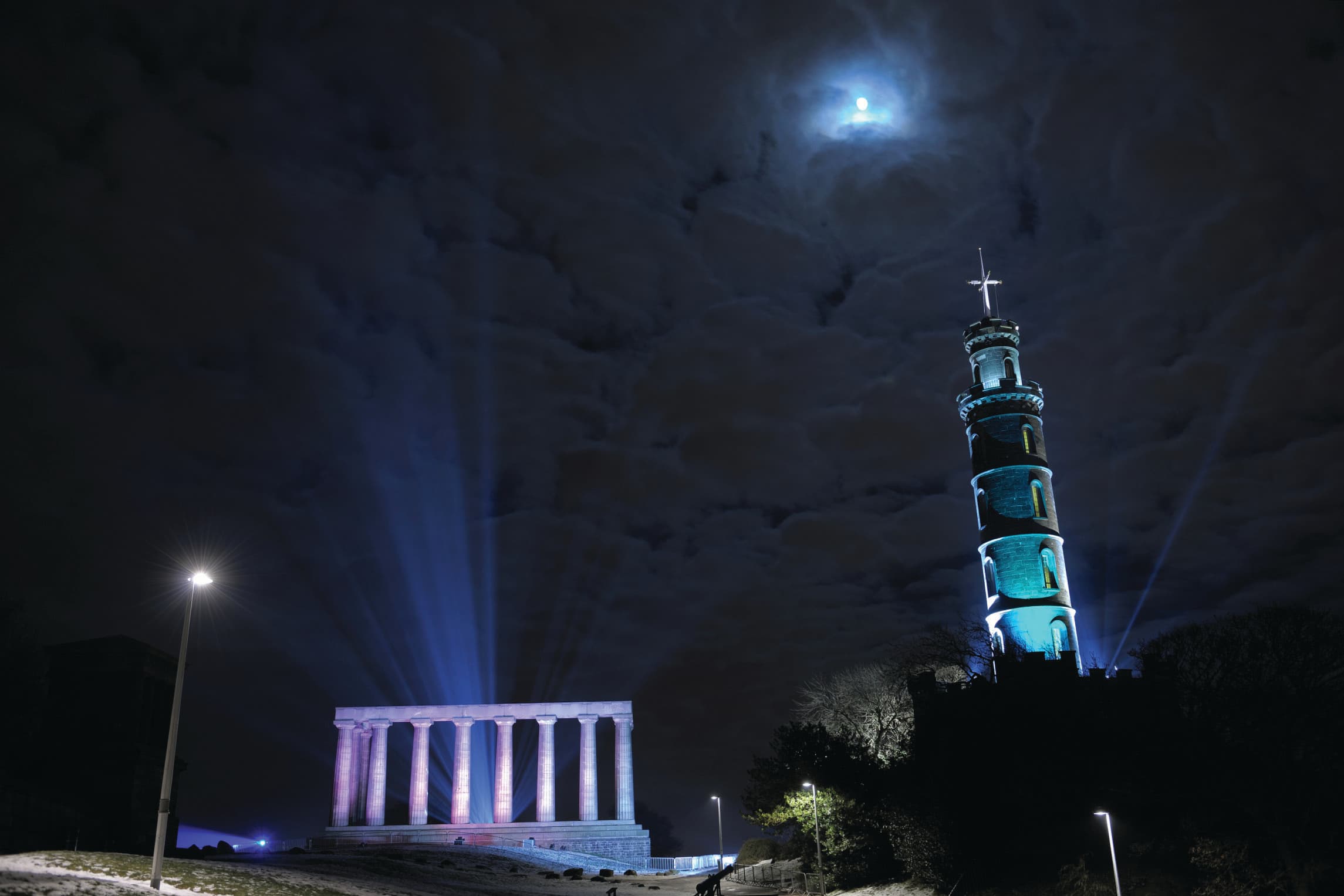 The striking Nelson monument showing the tall tower, showcasing a colorful light display against the night sky.