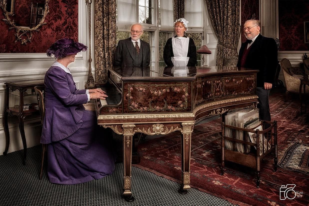 Women in Edwardian dress seated at a piano 