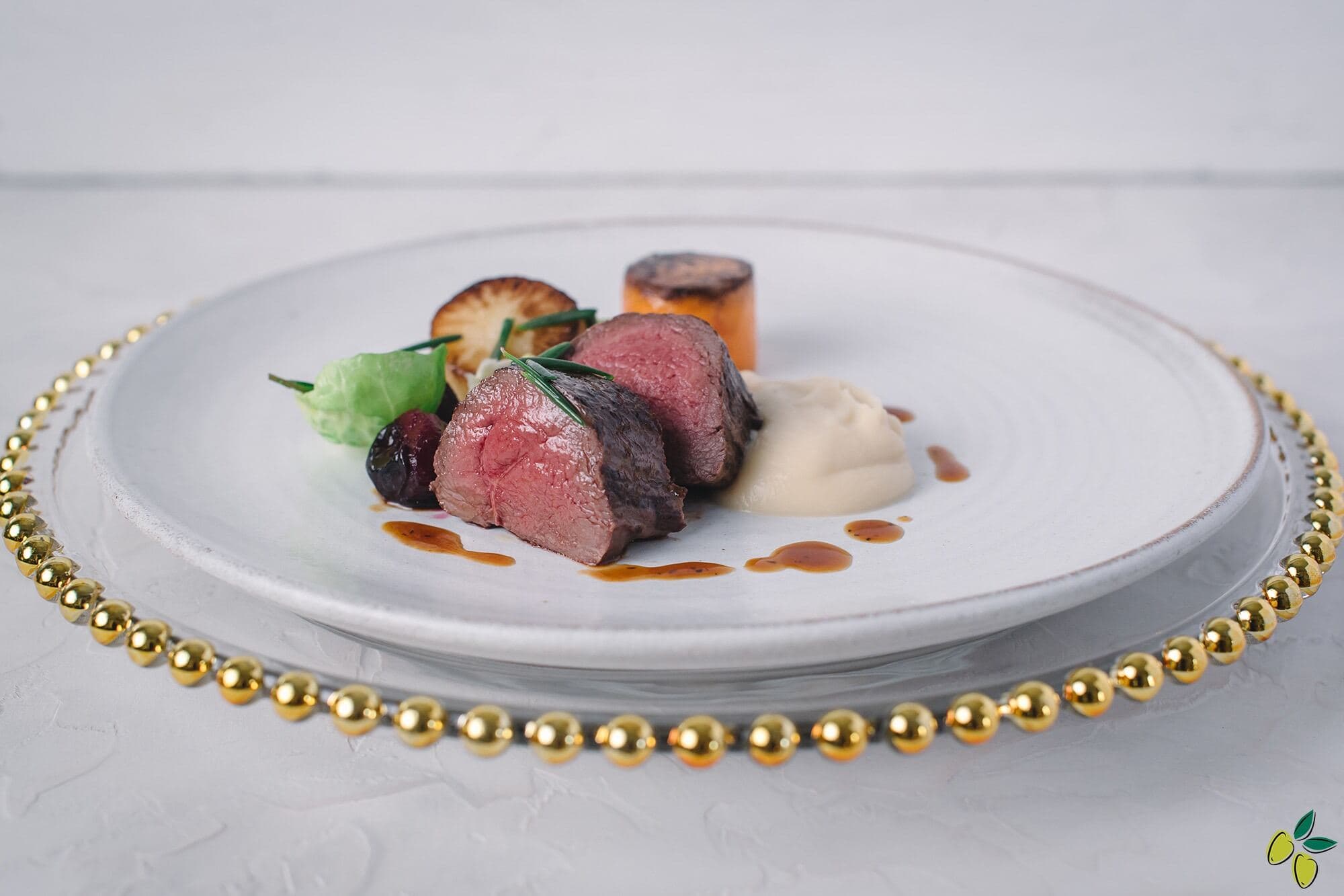 A plate featuring a portion of meat accompanied by a variety of colorful vegetables. And a row of gold beeds around the plate on the table