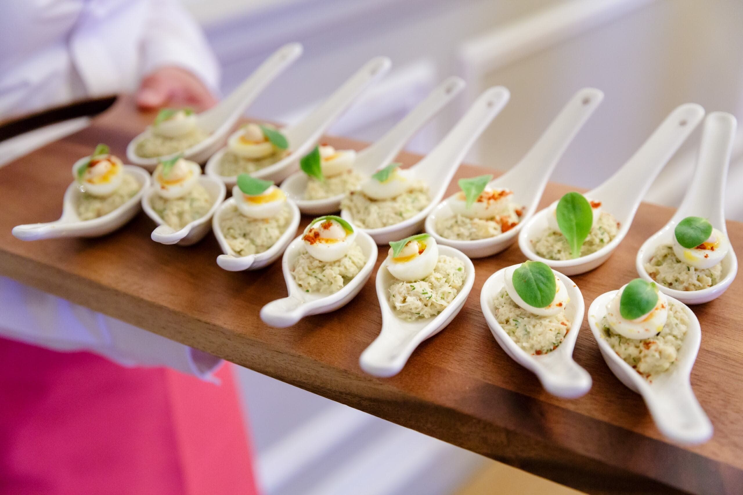 A woman holds a tray filled with small spoons, showcasing a variety of designs and finishes.