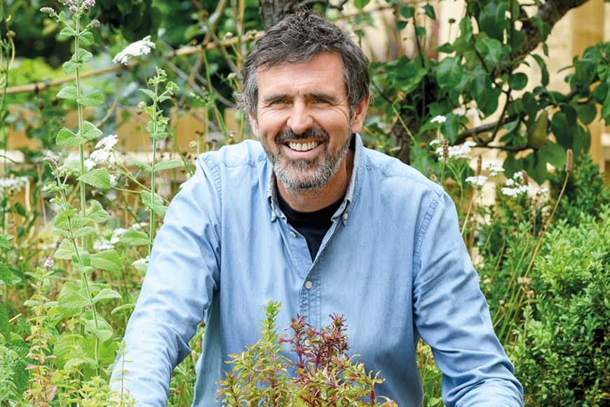 Adam Frost in a blue shirt surrounded by plants