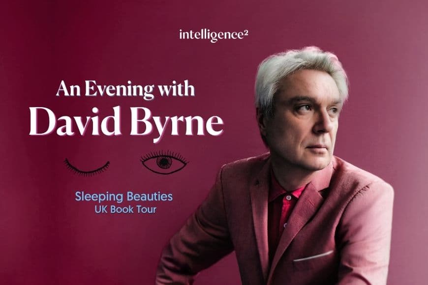 Image shows David Byrne wearing pink suit looking somber  