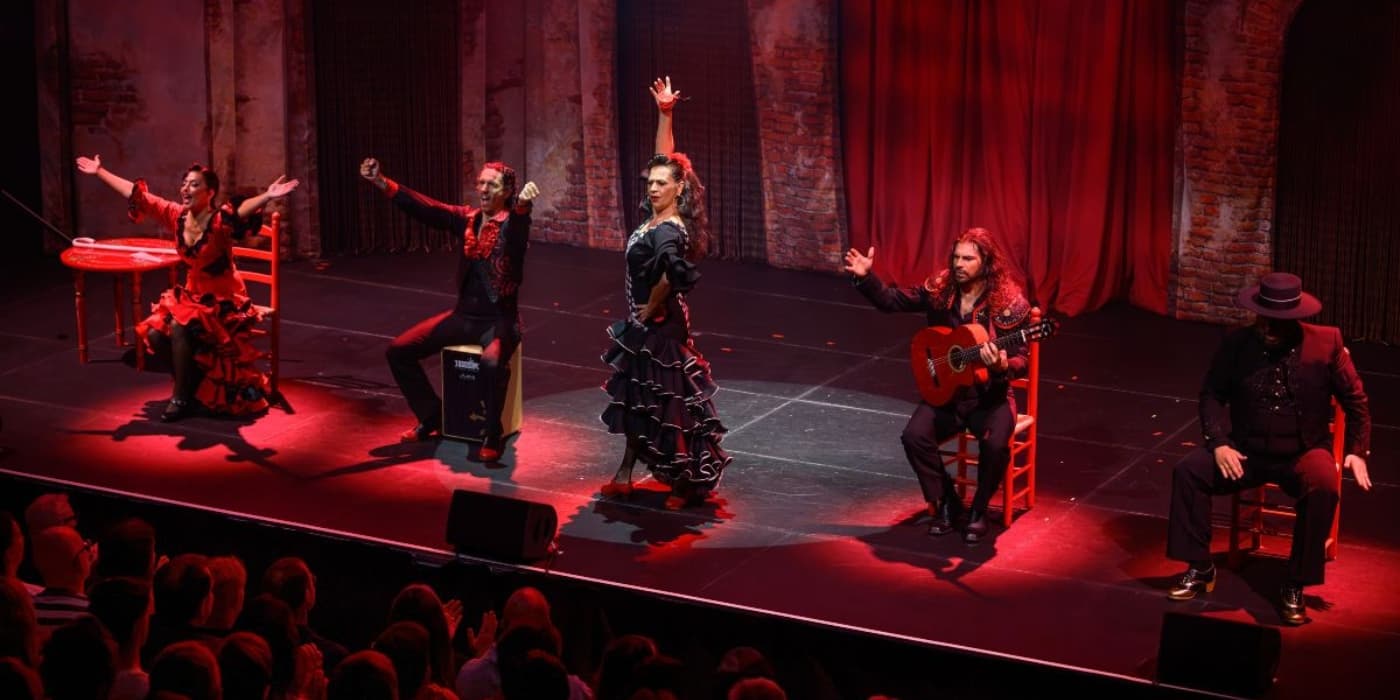 Flamenco dancers and band performing live to an audience under red lights
