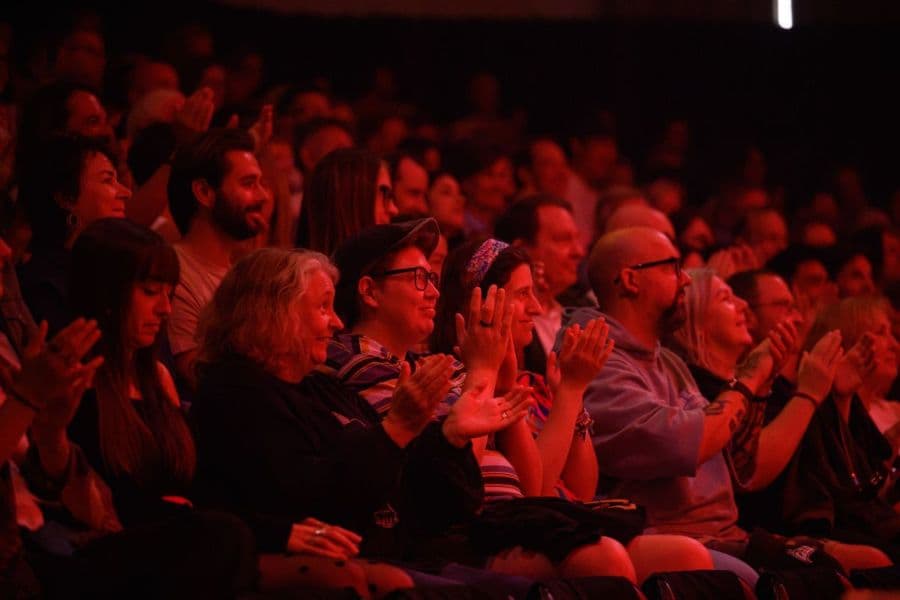 Crowd happily clap performers under red lights