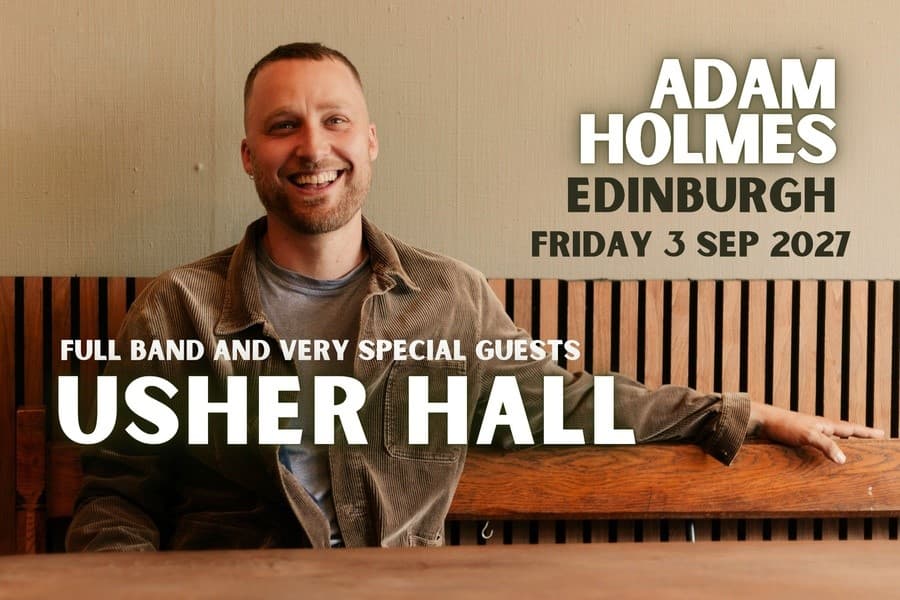 Adam Holmes seated wearing brown cord shirt, smiling.