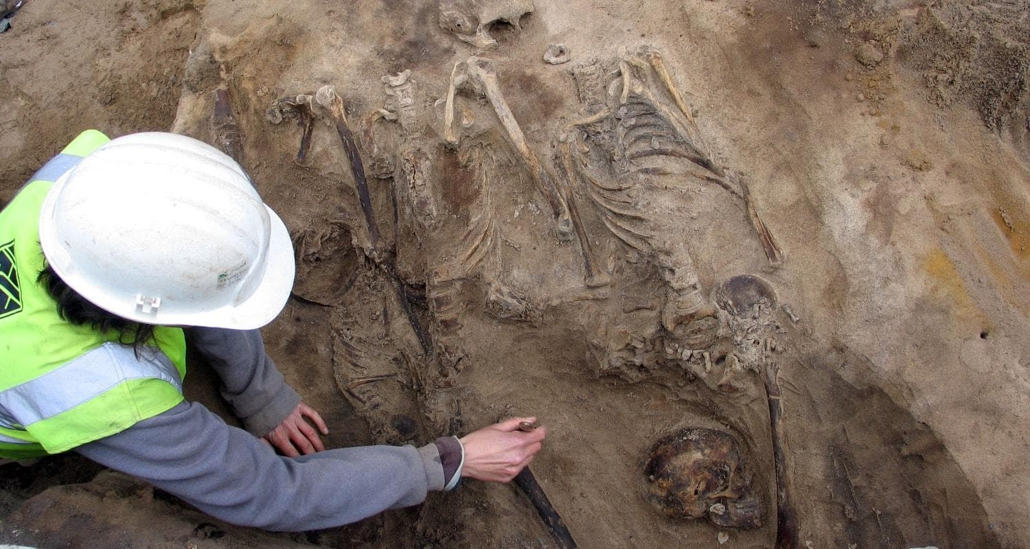 A person in a hard hat and safety vest inspects a human skeleton outside