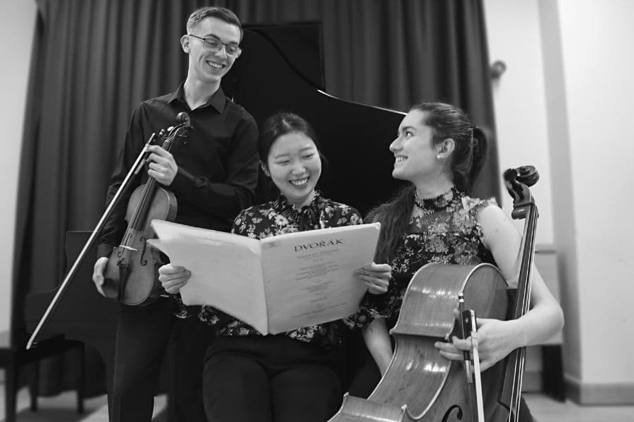 Image shows three musicians holding instruments and sheet music while smiling