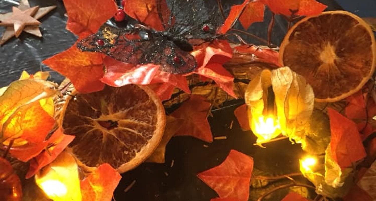 A festive wreath featuring autumnal leaves and circular orange slices, ideal for seasonal decoration.