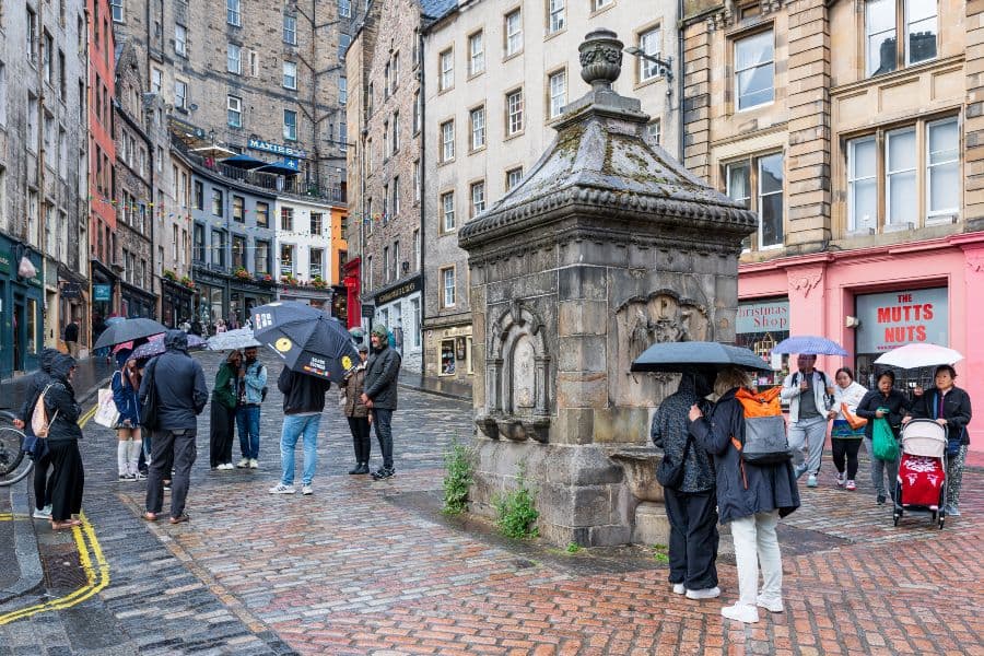 Tourists sheltering under umbrellas next to Bow Well in Edinburgh