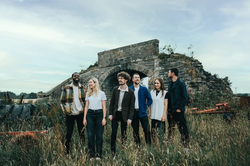 Celtic Worship band members stood in front of an old stone foot bridge ruin