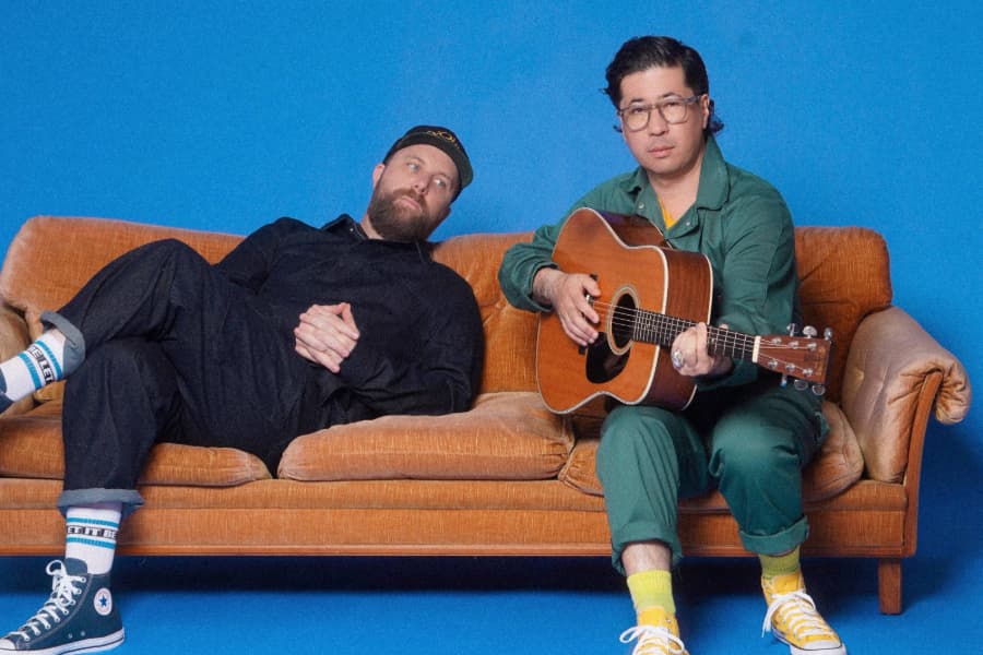 Daveed Goldman and Nobu Adilman sitting on a couch with a guitar