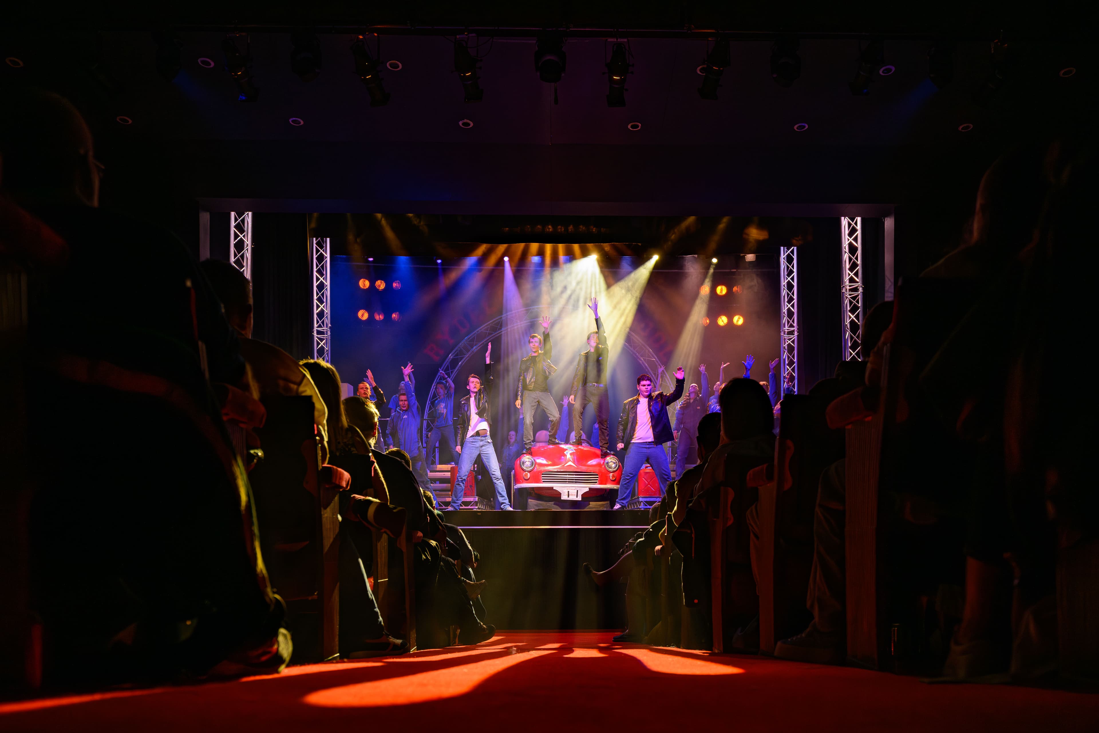 A stage showing a performing show. An audience is seated in chairs, ready for a performance or presentation.