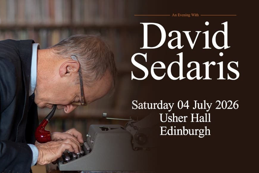 David Sedaris smoking a pipe whilst he leans over his typewriter