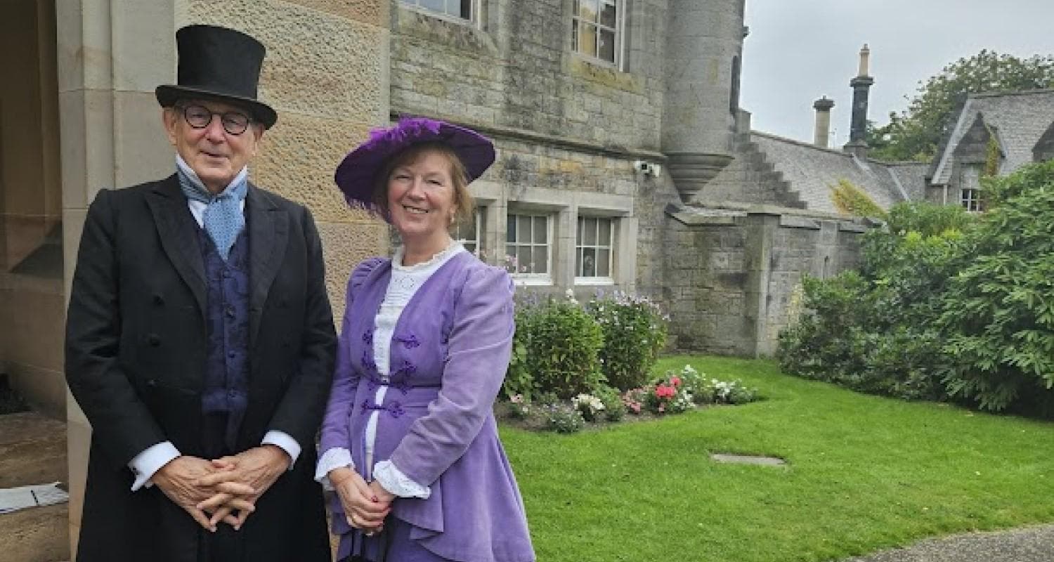 A couple dressed in Edwardian costume smile at the camera outside Edinburgh's Lauriston Castle