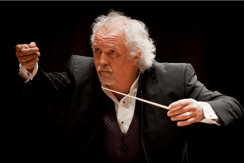 Close up photograph of conductor Donald Runnicles leading an orchestra with his arms outstretched holding a baton. Part of the Edinburgh International Festival 2026