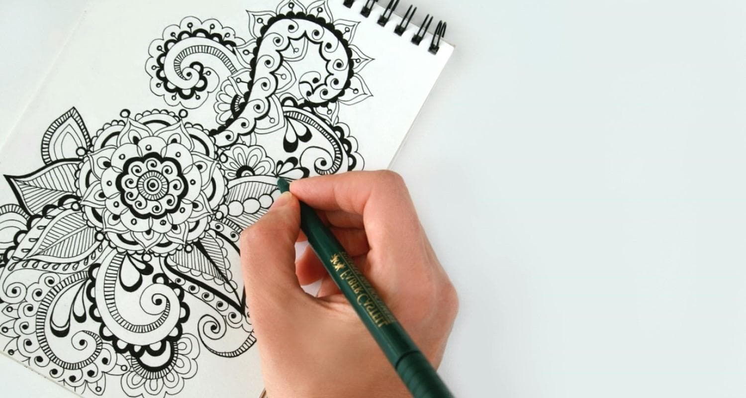 A person is drawing a detailed flower design in a notebook