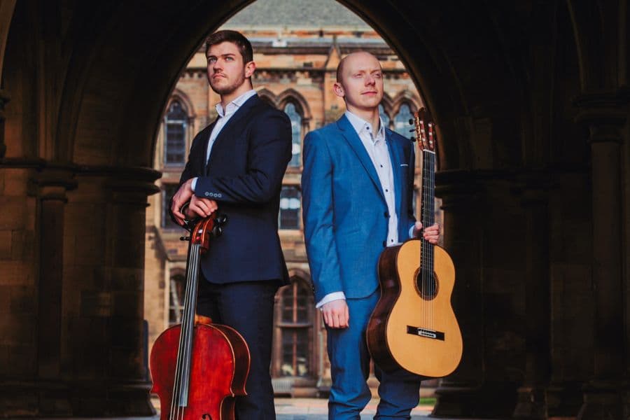 Image shows two men standing with a guitar and cello
