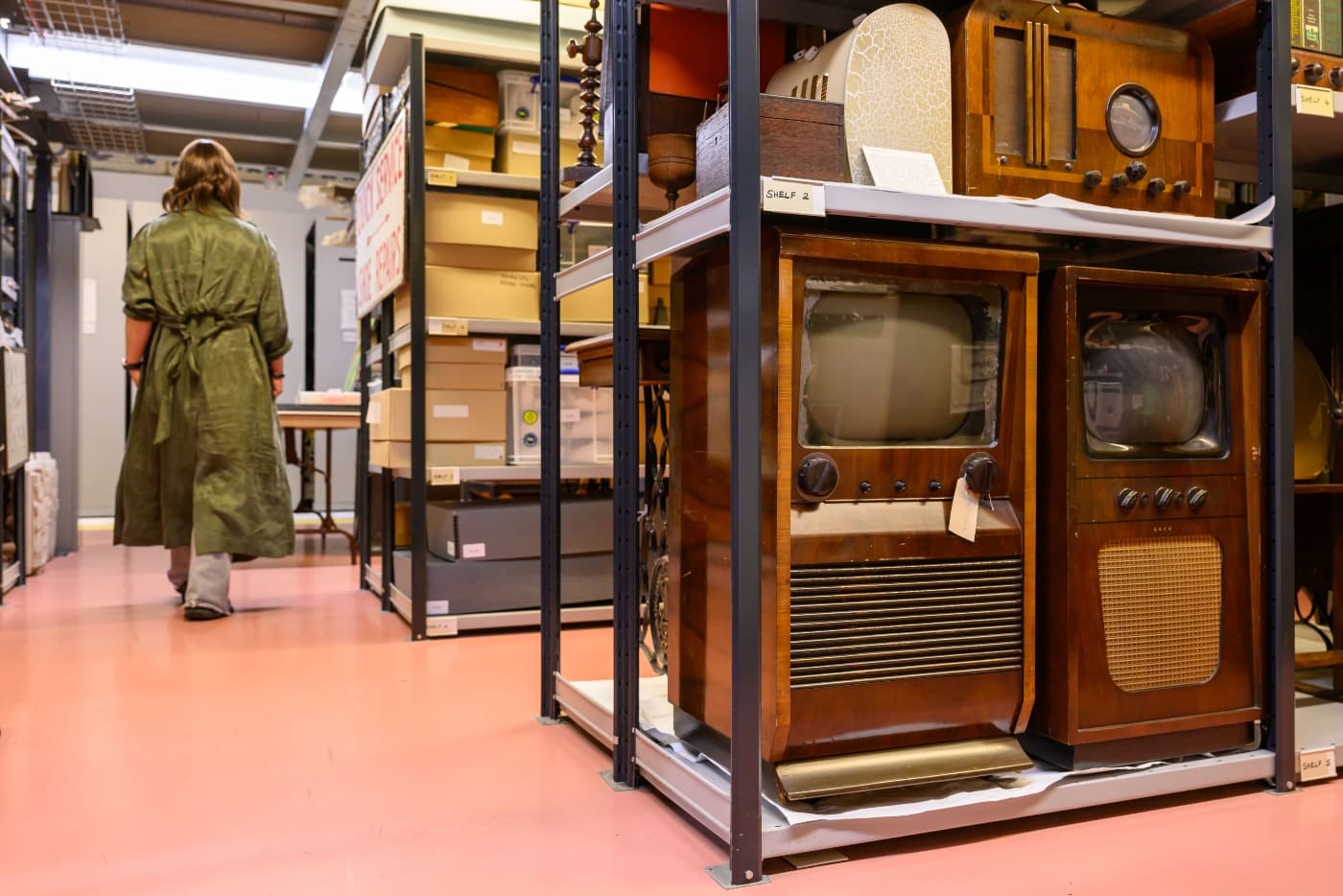 A visitor walks through the Museum Collections Centre in Edinburgh. The room is filled with vintage televisions from various decades.