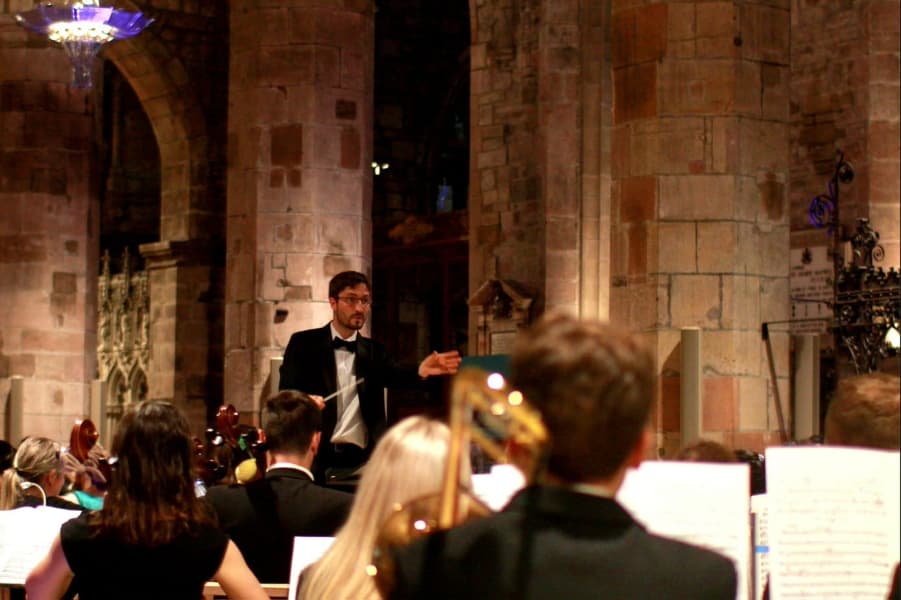 Image shows members of Edinburgh City Orchestra playing instruments with a conductor