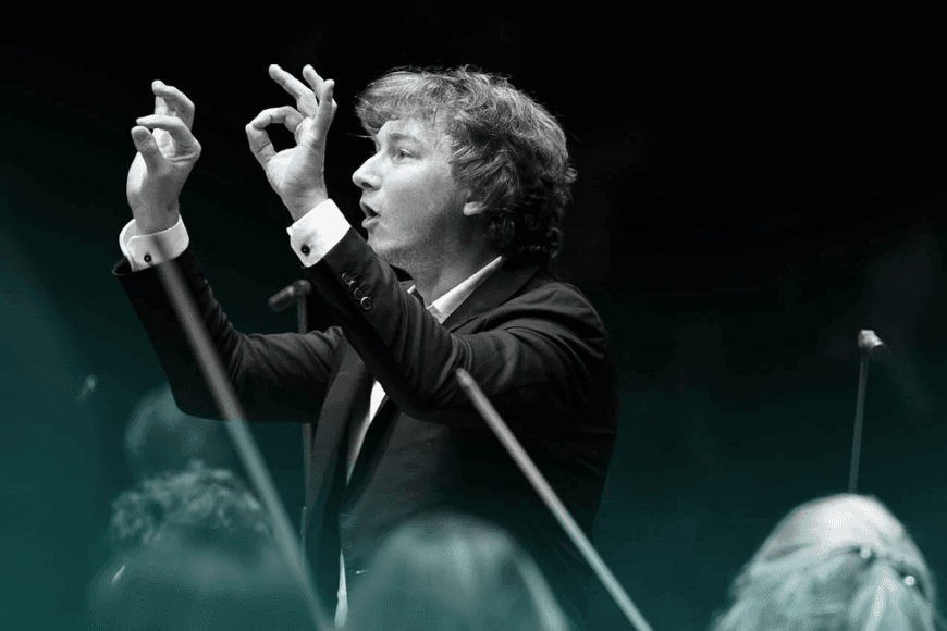 Black and white photograph of conductor Maxim Emelyanychev with blue colour wash