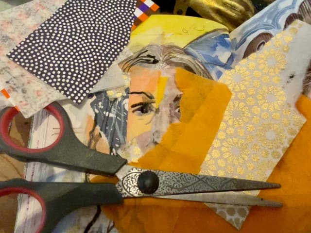 A pair of scissors rests beside pieces of fabric and a drawing of a face.