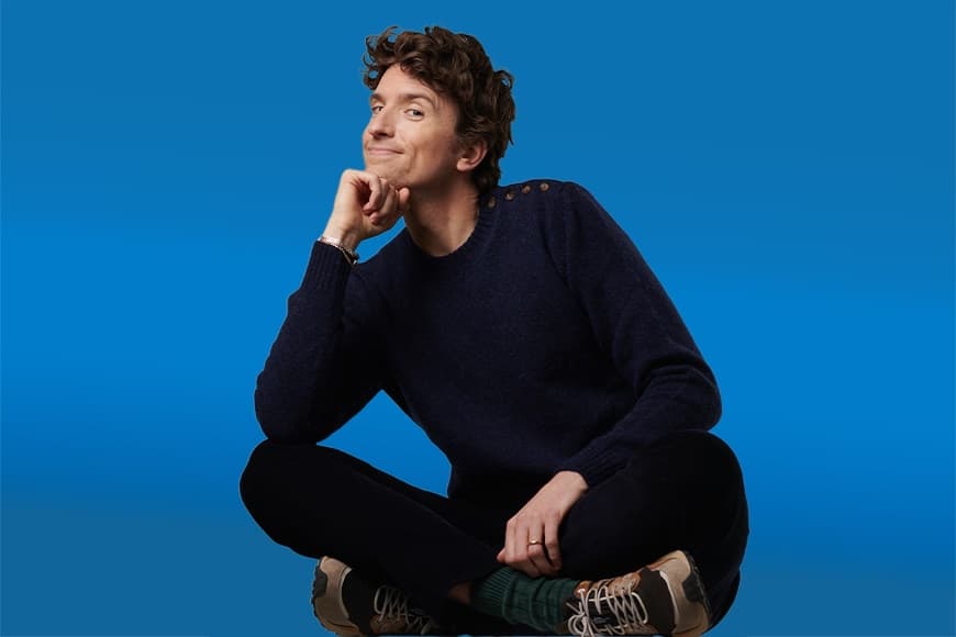 Greg James sat crossed legged on the floor with his chin resting on his hand 