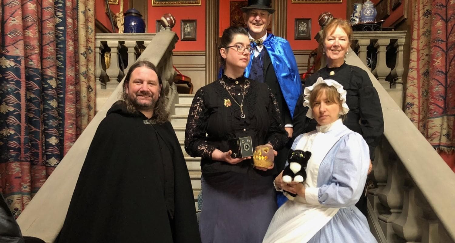 A group of individuals dressed in Edwardian costume pose together for a photograph on the stairs in Lauriston Castle