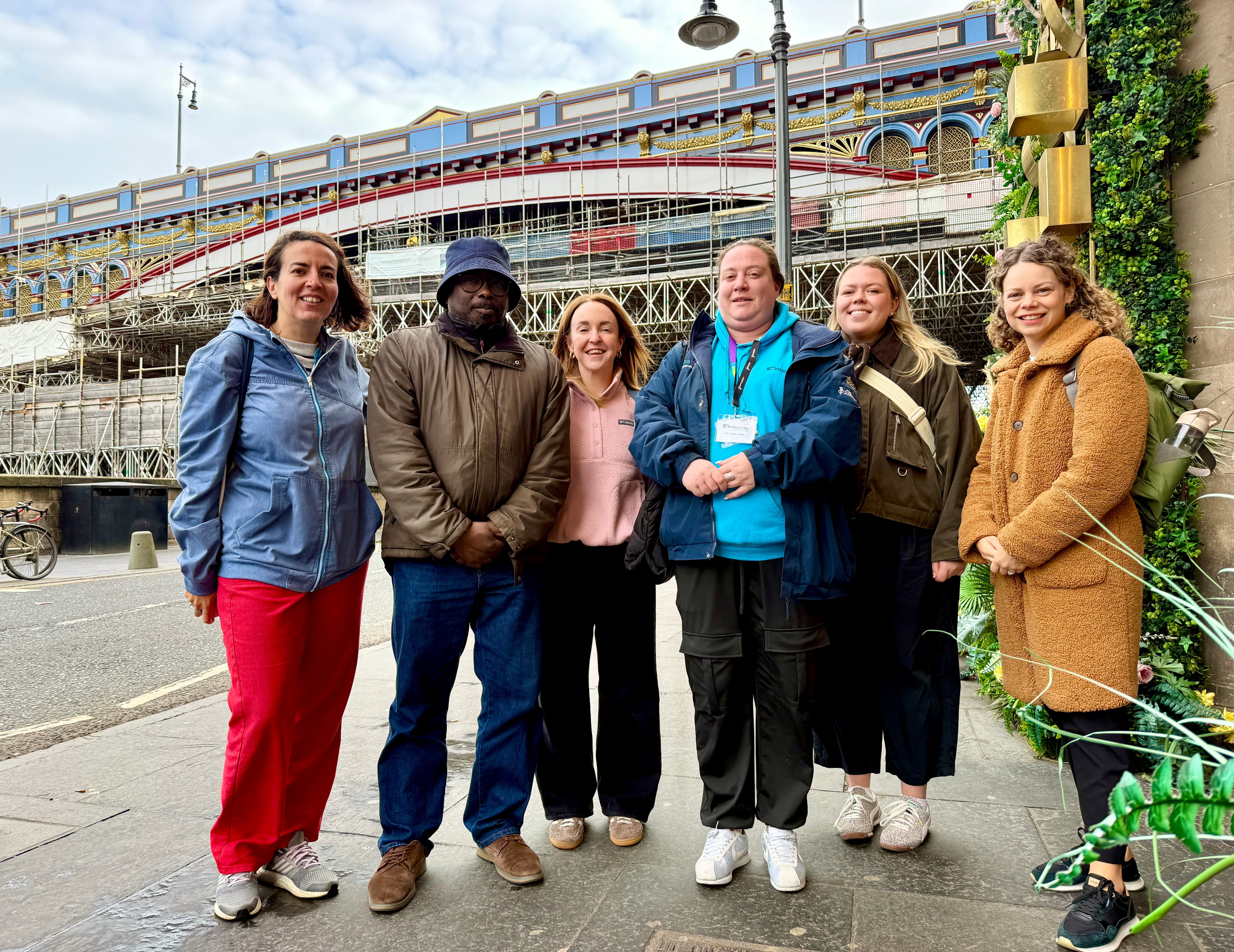 Group of six people posing for a photo with a bridge in the background