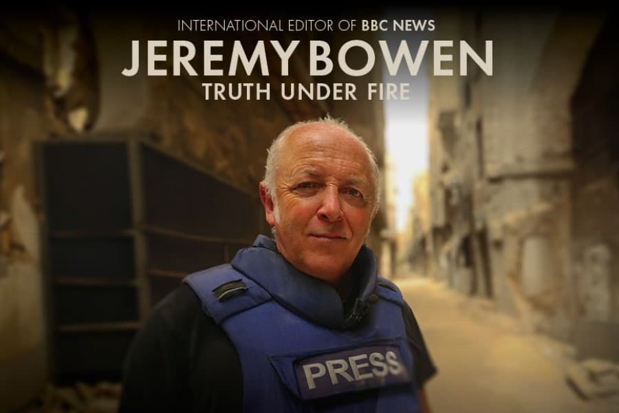 Jeremy Bowen looking straight to camera wearing a flack jacket with the word press on the front