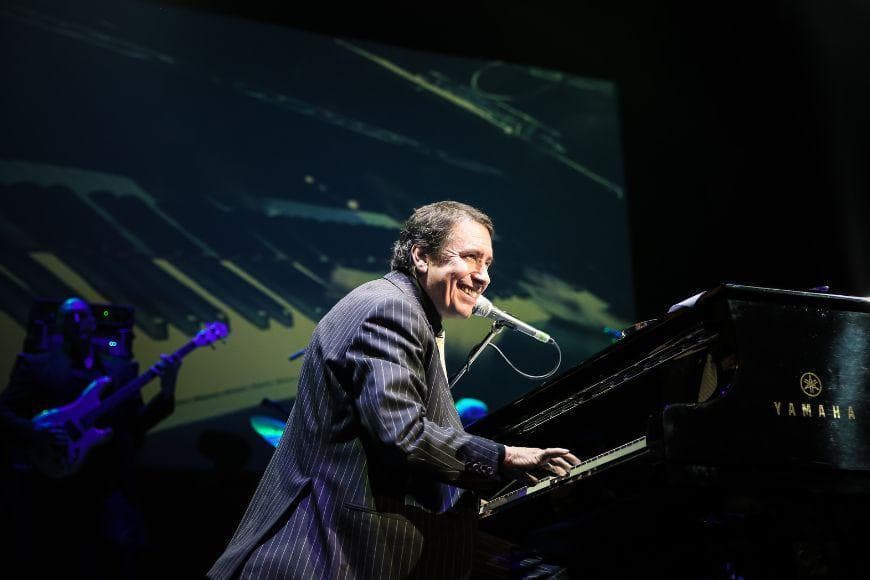 Jools Holland sitting at a piano singing during concert