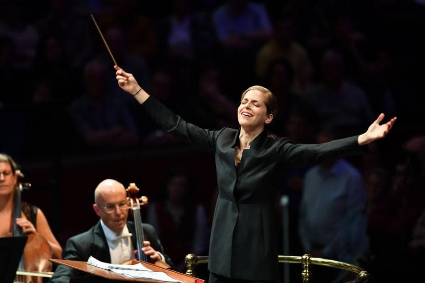 Karina Canellakis on stage arms stretched wide, conducting