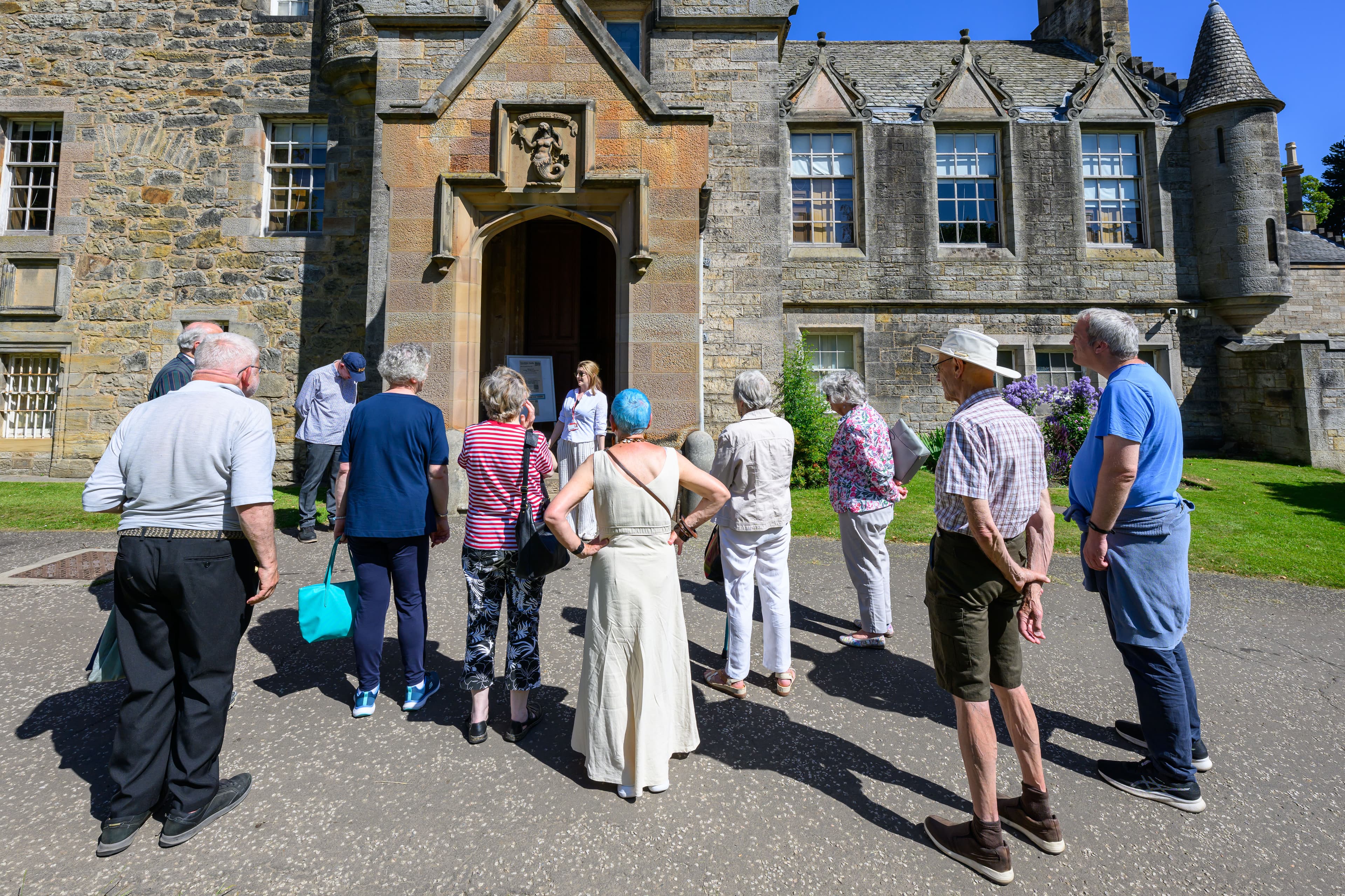A diverse group of people poses outside a historic castle, with its tall towers and walls visible in the background.