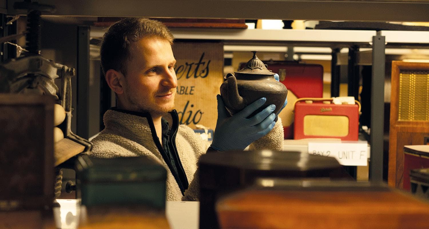 A curator at Edinburgh's Museum Collections Centre holds a vintage teapot in both hands.