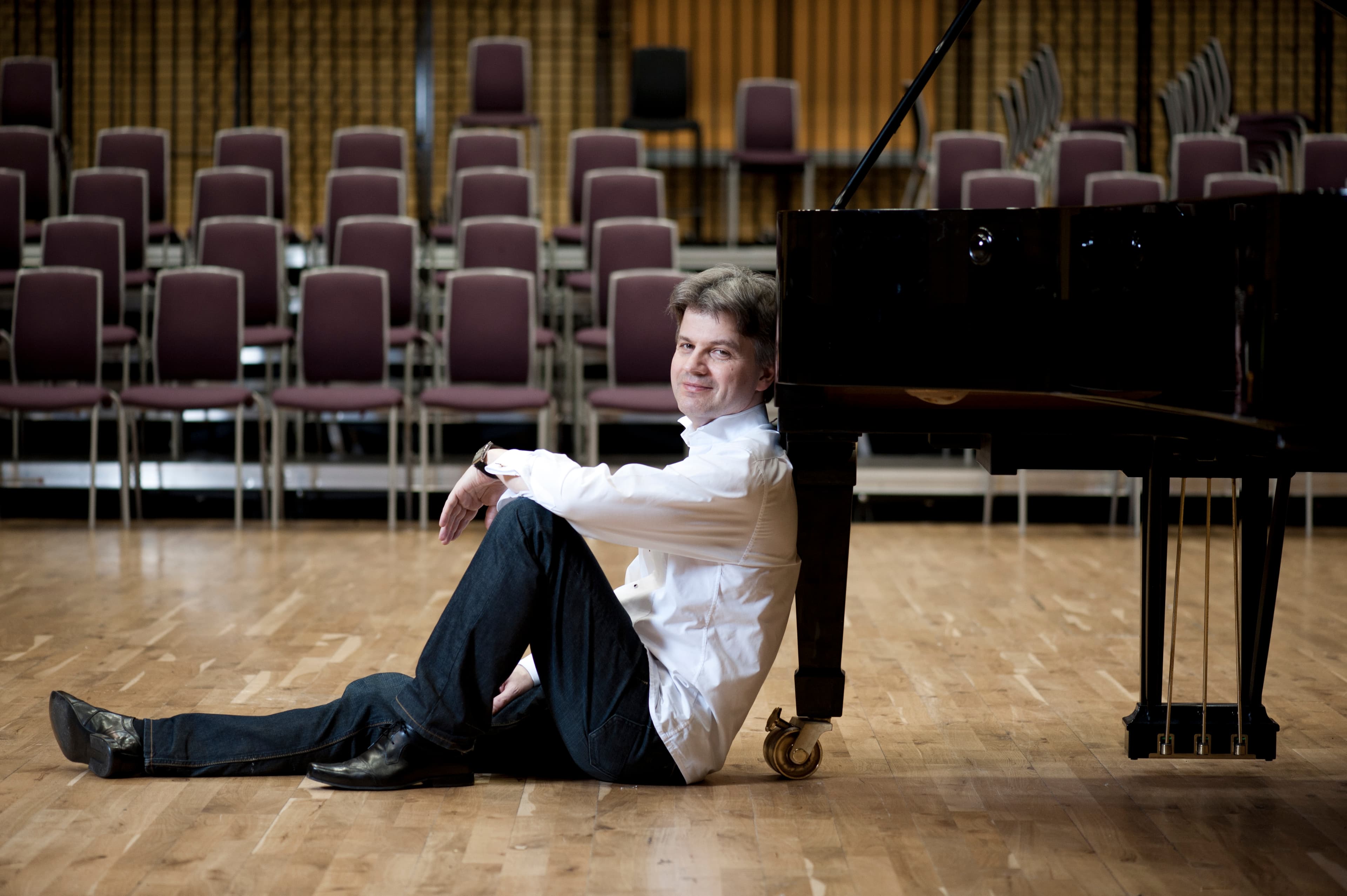Pianist, Mark Bebbington sitting on the floor leaning against the leg of a piano.