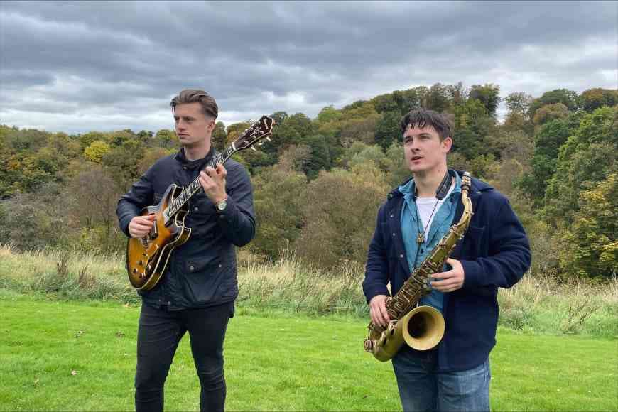 Saxophonist Matthew Kilner and guitarist Kevin Henderson photographed side by side in a field.