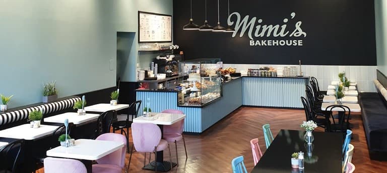 Interior of Mimi's Bakehouse located in Edinburgh's City Art Centre. Pink and blue chairs are arranged for customers around black tables, creating an inviting atmosphere.