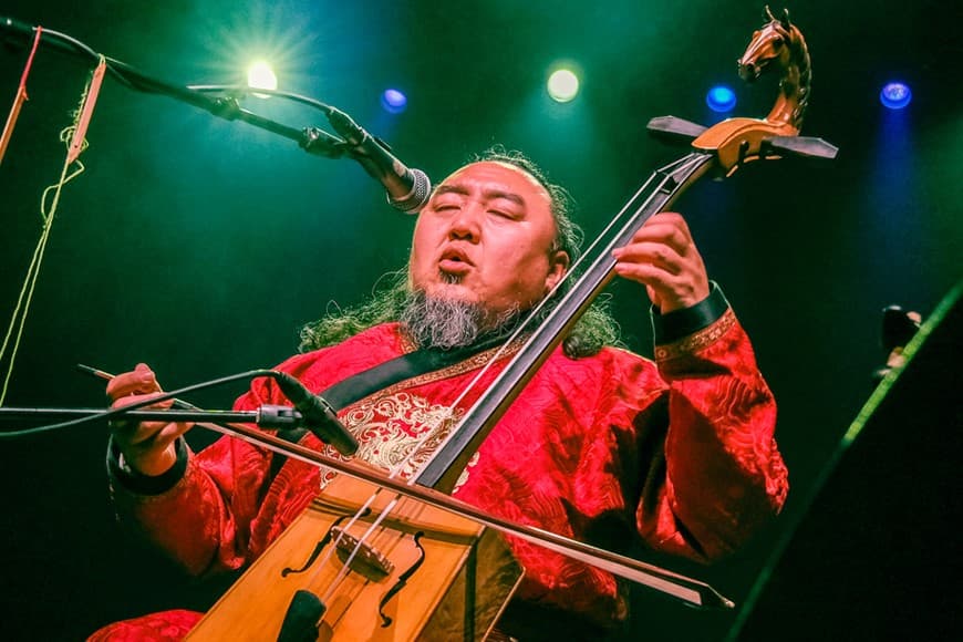 Image shows man singing into microphone while playing instrument