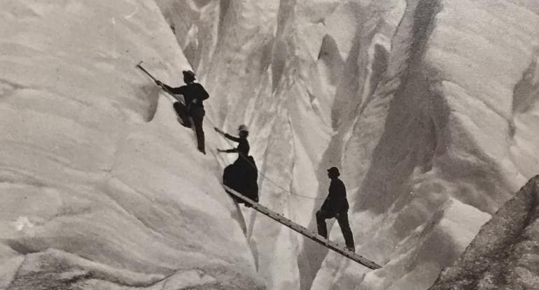 Vintage black and white image of men and women scaling an icy mountain in period dress