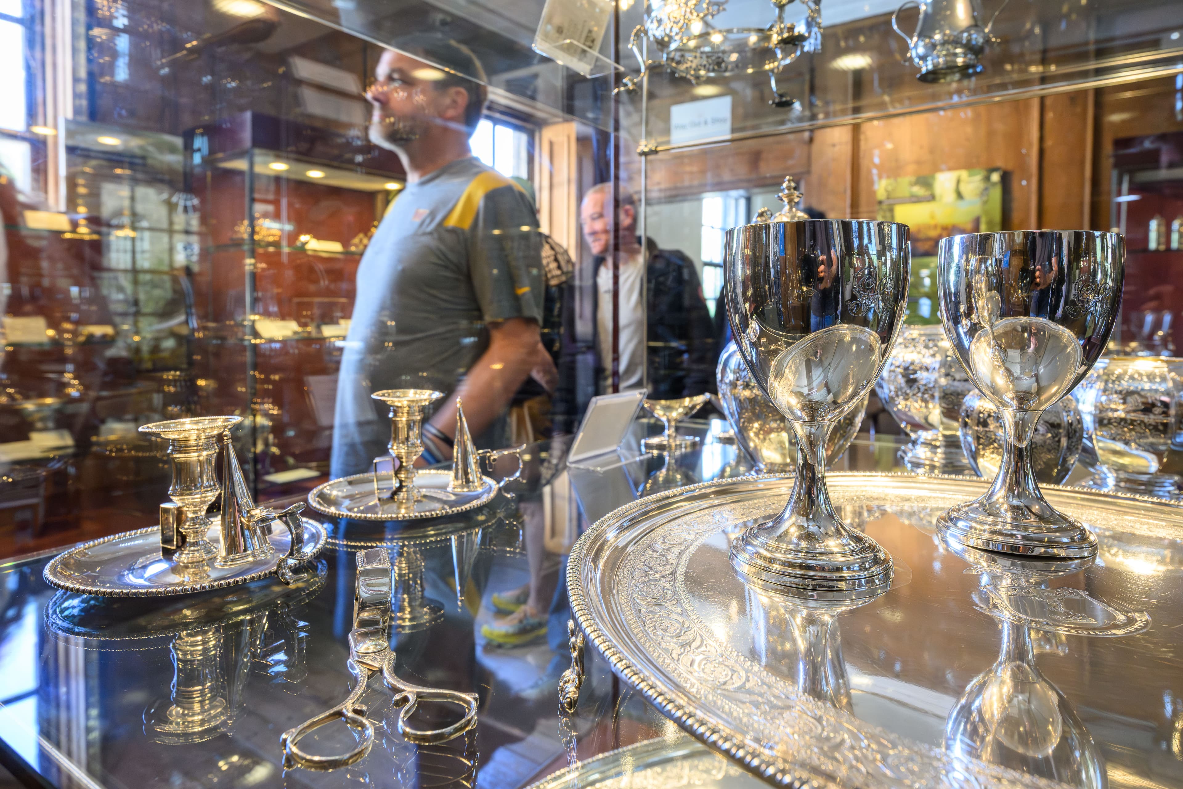 A visitor examines silver items displayed in a glass case, showcasing intricate designs and craftsmanship.
