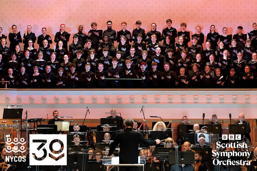 Image shows NYCOS singing on stage with orchestra and conductor