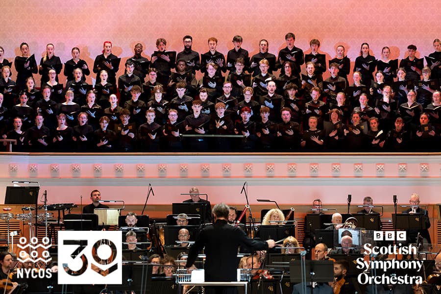 Image shows NYCOS singing on stage with orchestra and conductor