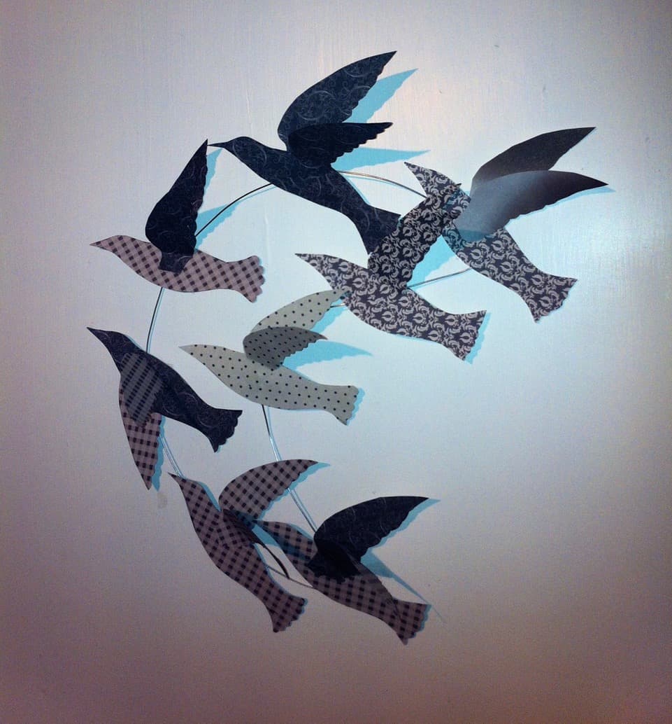 A decorative wall hanging featuring paper birds arranged on a wire