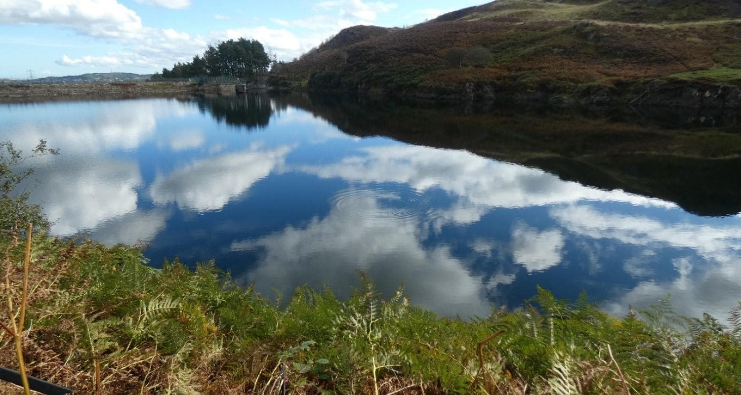 A calm lake mirrors white clouds above, creating a tranquil and picturesque landscape.