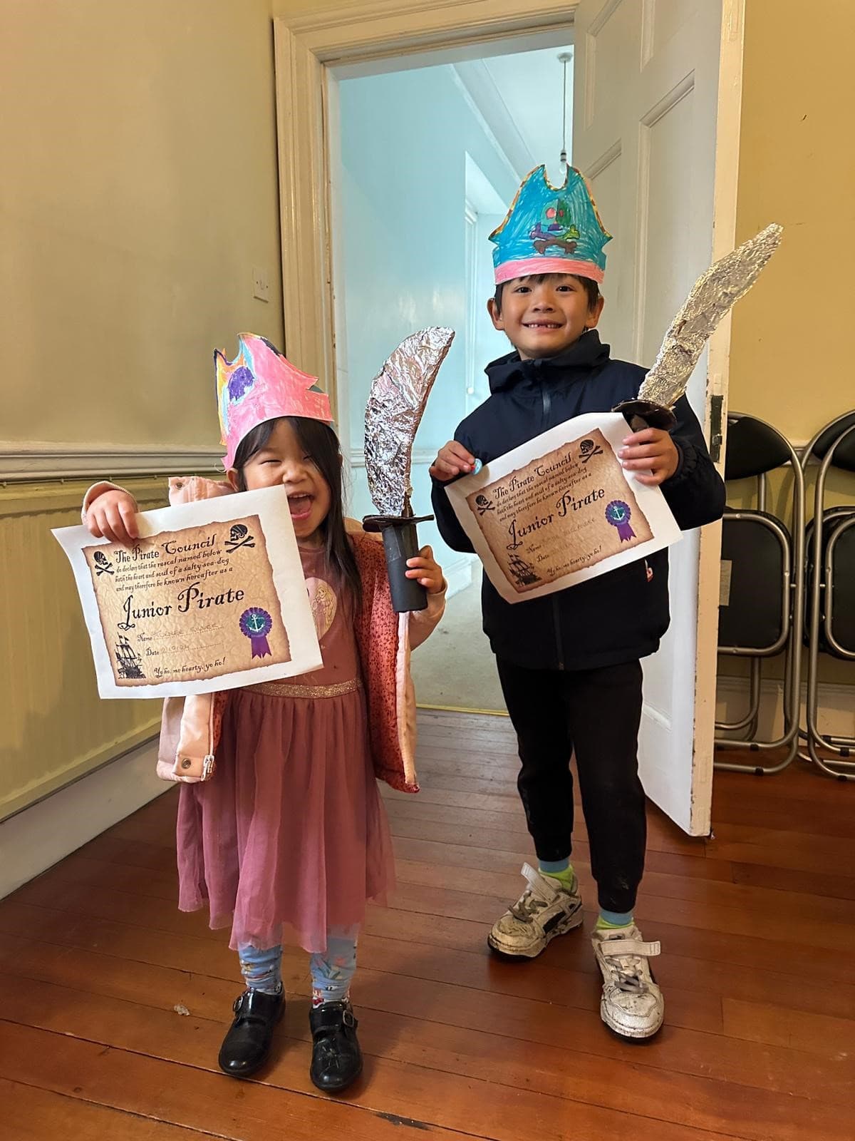 Two children proudly hold certificates while wearing colourful pirate hats.