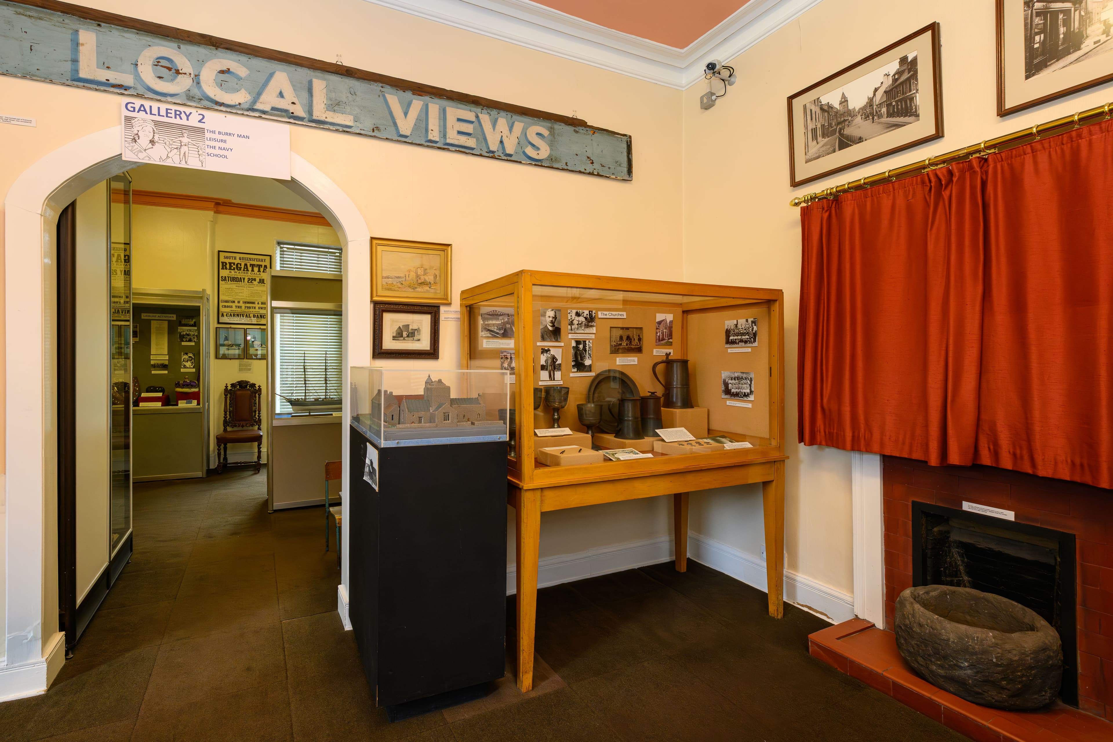 A cozy museum room featuring a fireplace and a sign reading "Local Views" on the wall. A case with items of interest is in the corner.