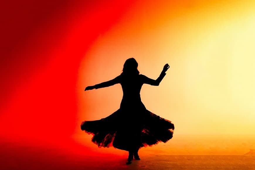 Image shows shadow of woman dancing with sunset coloured backdrop