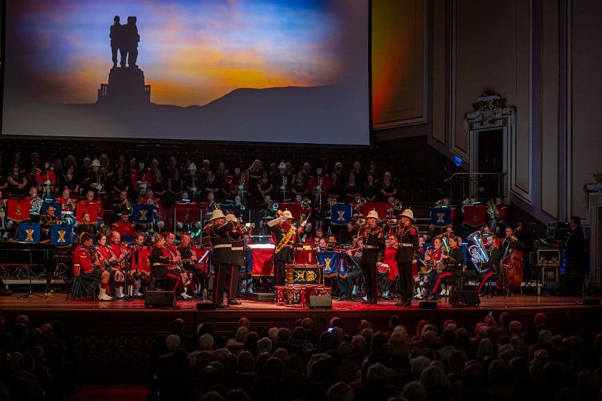 Image of orchestra on Usher Hall stage with a screen in hte background showing to soldiers standing on a hill