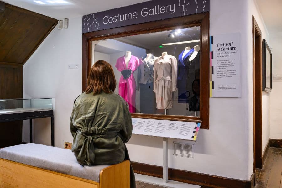 A woman stands in front of a clothing display, looking at various garments with interest.
