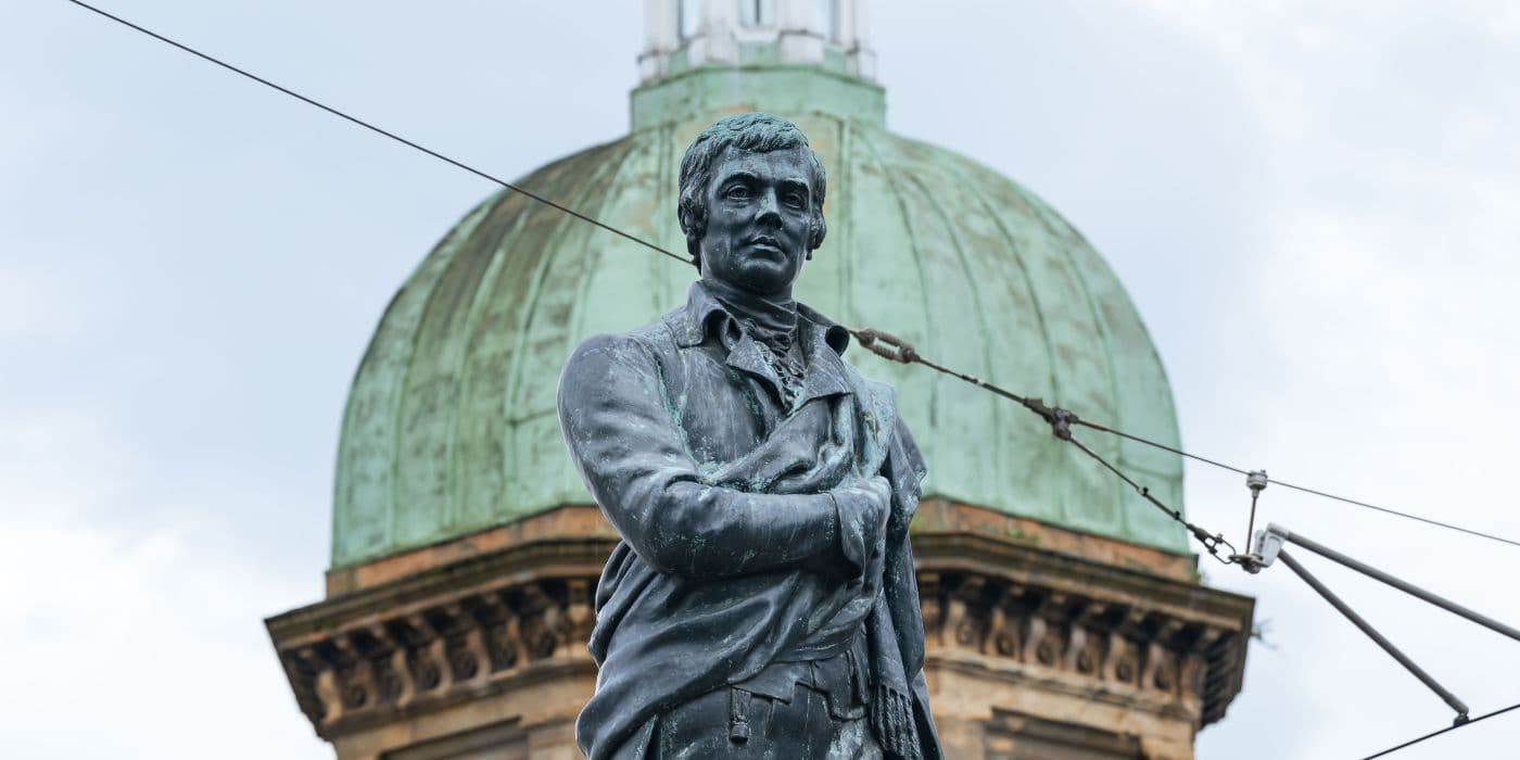 Statue standing proudly with the green dome of a building in the background