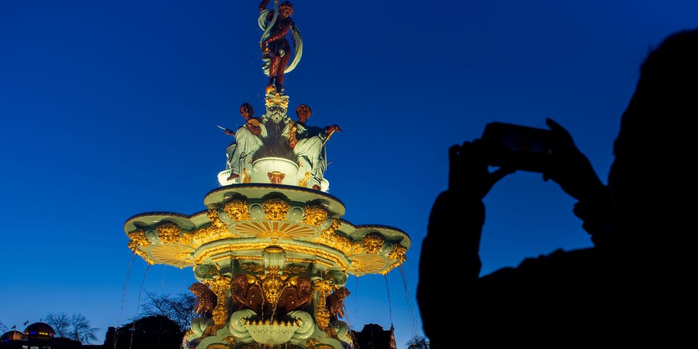 Night time shot of the Ross fountain lit up with the silhouette of someone taking a photo